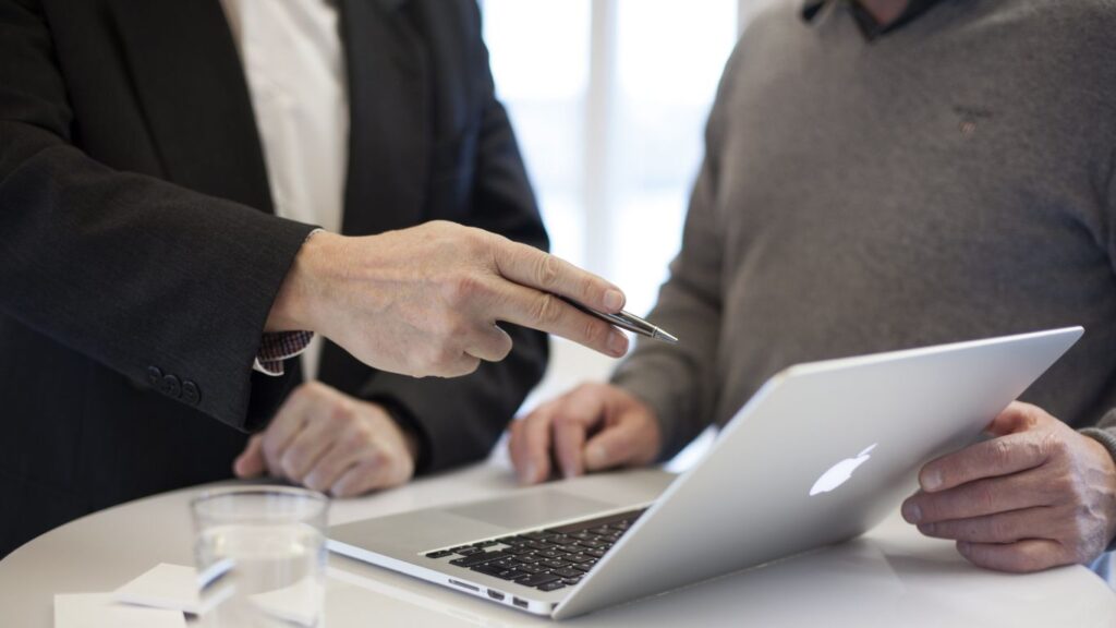 Two men talking and looking at a laptop.